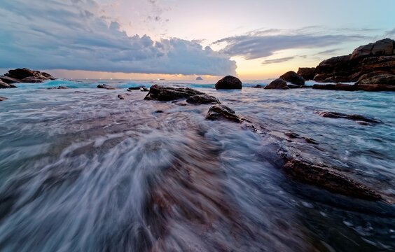 Beautiful sunrise scenery of a rocky beach on northern coast of Taiwan, with golden sun rising on distant horizon & turbulent waves beating on rugged rocks under dramatic dawning sky (Long Exposure)