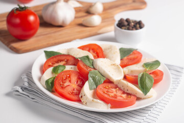 Delicious Italian caprese salad with sliced mozzarella, tomatoes, basil, pesto and garlic on background.