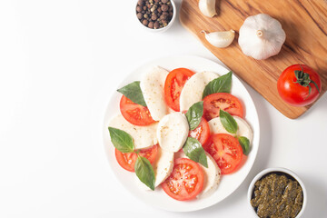 Delicious Italian caprese salad with sliced mozzarella, tomatoes, basil, pesto and garlic on background.