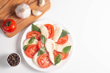 Delicious Italian caprese salad with sliced mozzarella, tomatoes, basil, pesto and garlic on background.