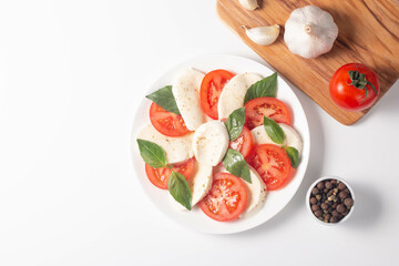 Delicious Italian caprese salad with sliced mozzarella, tomatoes, basil, pesto and garlic on background.