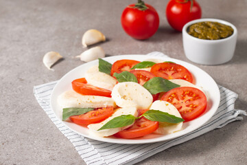 Delicious Italian caprese salad with sliced mozzarella, tomatoes, basil, pesto and garlic on background.