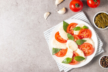 Delicious Italian caprese salad with sliced mozzarella, tomatoes, basil, pesto and garlic on background.