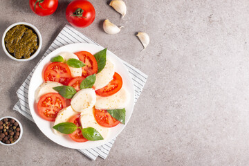 Delicious Italian caprese salad with sliced mozzarella, tomatoes, basil, pesto and garlic on background.