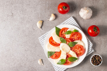 Delicious Italian caprese salad with sliced mozzarella, tomatoes, basil, pesto and garlic on background.