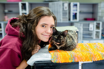 Brunette Teen Smiles at Camera with a Cat at a Shelter - obrazy, fototapety, plakaty