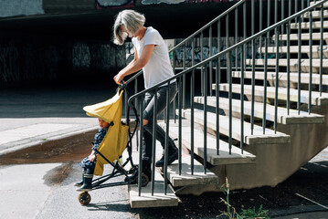 Woman lifts stroller on steps of street stairs and lack of ramp