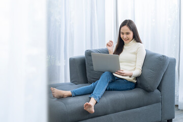 Young pretty Asian woman sitting on sofa. Young Asian woman working with a laptop computer sitting on the cozy sofa.