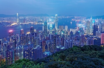 Night scenery of Hong Kong viewed from Victoria Peak with city skyline of crowded skyscrapers by Victoria Harbour and Kowloon area across seaport ~ Beautiful cityscape of Hong Kong in blue twilight