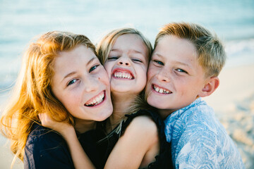 Pre-teen and child siblings hug and snuggle smiles on beach vacation