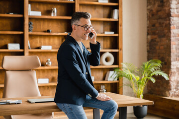 Caucasian mature middle-aged businessman ceo boss freelancer talking on smart phone cellphone with clients consulting customers online in office