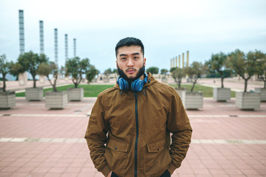 Serious ethnic man with headphones on neck in city park