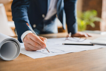 Cropped closeup photo of male architect engineer working on construction plan, dealing with blueprints on table at office. Building construction industry