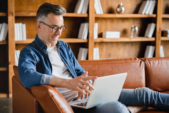 Remote work on distance. Caucasian mature middle-aged man businessman freelancer working on laptop, watching webinars, e-learning, multitasking on the sofa at home office