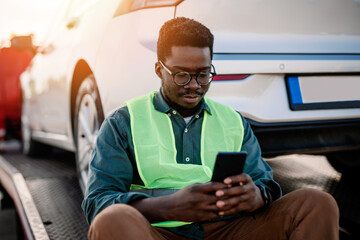 Young African American man reports by phone that his car broke down and that he called the towing...