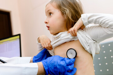 Doctor examining heartbeat of a little girl by stethoscope - obrazy, fototapety, plakaty