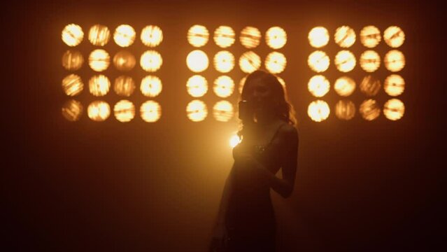 Silhouette girl musician singing mic in studio lights. Woman performing on stage