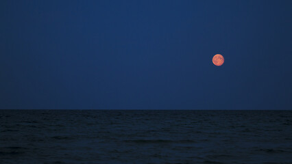 The rising red moon over the dark blue Baltic Sea
