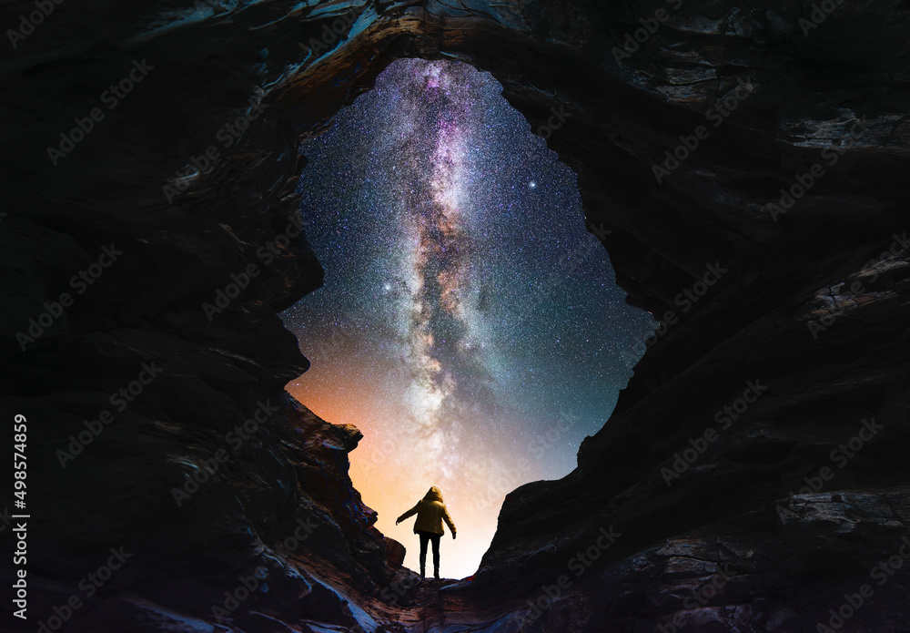Wall mural silhouette of a person in the cave looks on the bright milky way galaxy. fantasy scene.