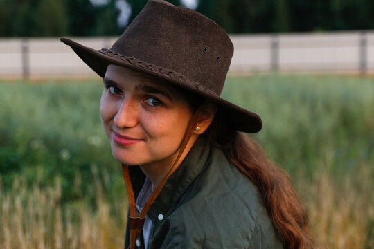 Defocus portrait smiling young woman in cowboy hat. Girl in a cowboy hat in a field. Nature background. Closeup portrait caucasian girl smiling. Summertime emotion. Fashion clothes. Out of focus