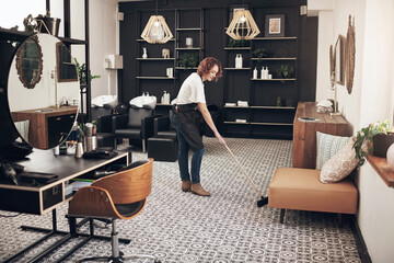 A clean space is a happy space. Shot of a hairstylist sweeping the salon.