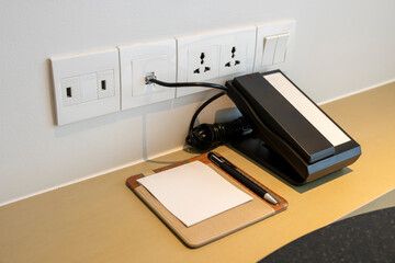 White power socket and switch with black phone and note paper and pen in resort bedroom. Give a...