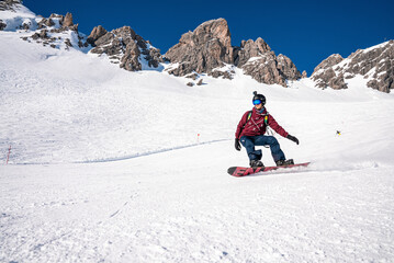 Fototapeta na wymiar St. Anton am Arlberg. March 10, 2022. Young snowboarder sliding down slope on snow covered mountain at ski resort during beautiful sunny day, Male snowboarder riding snowboard in mountain