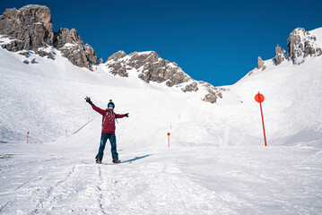 St. Anton am Arlberg. March 10, 2022. Young snowboarder with arms outstretched standing on mountain slope at ski resort, Male snowboarder rising his hands up on snowy mountain
