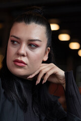 Close up photo of young beautiful woman. Her hand on chin. Bokeh lights at back. Black background.