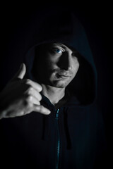 Shaka - Portrait of a young hooded man who in the shade makes a sign of relaxation with his hand, hang loose, salutation