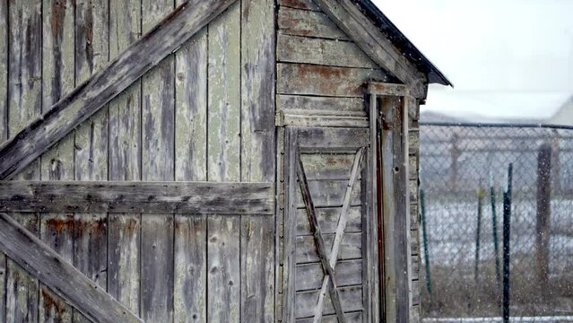 Snow falling in slow motion in front of old rustic wood barn shed in Wyoming.