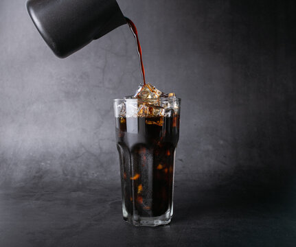 Pour coffee of americano coffee into a transparent glass with ice. and roasted coffee beans on a black background studio photo