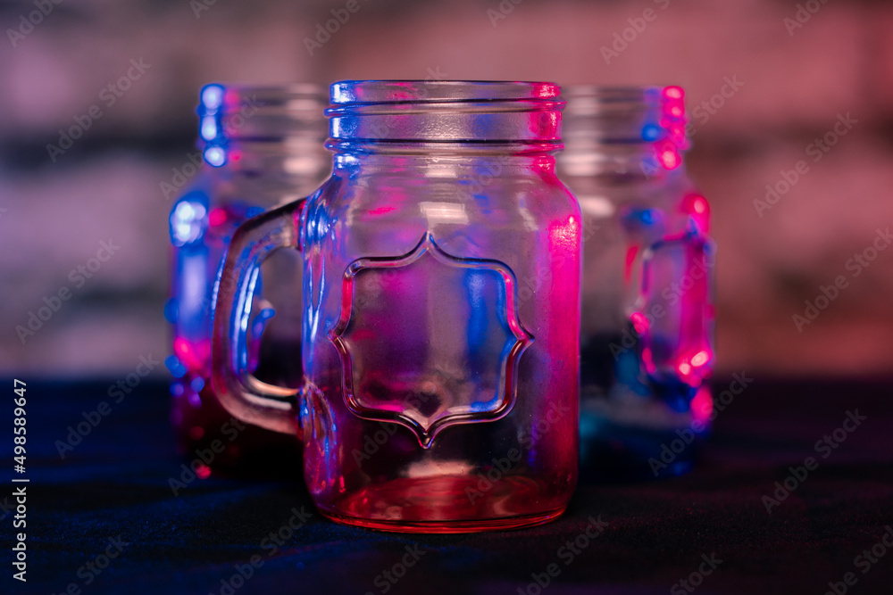 Poster closeup shallow focus shot of empty gradient color glass jars with a handle on a table