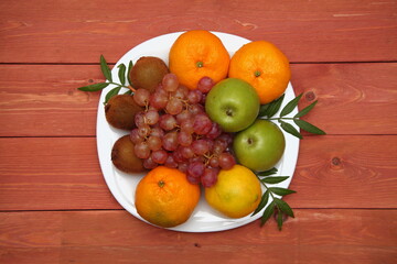 Fototapeta na wymiar Fruit concept. Kiwi, bunch of grapes, orange, green apple on a white plate. on wooden background