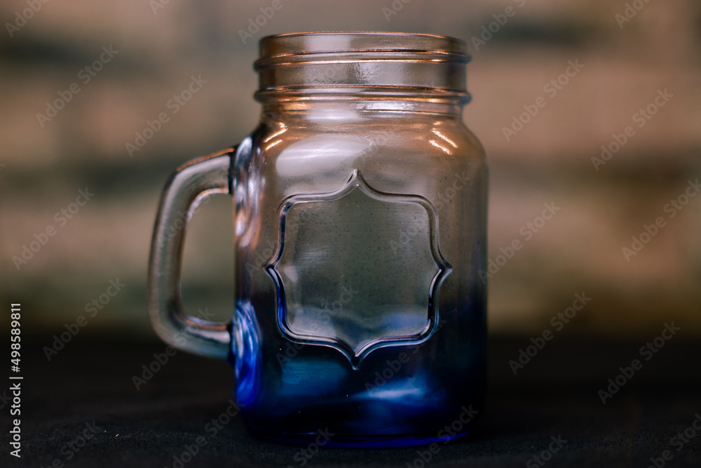 Poster closeup shallow focus shot of an empty gradient color glass jar with a handle on a table