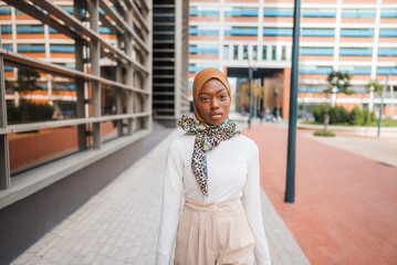 Stylish black woman in headscarf standing on street