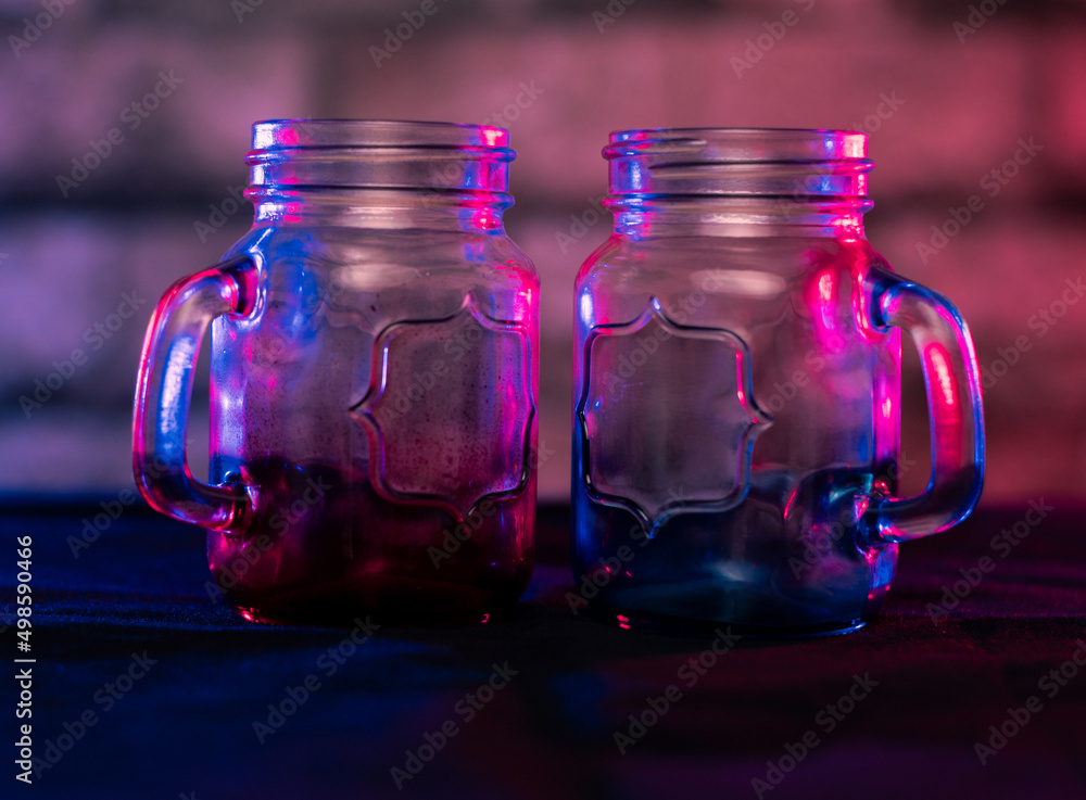 Poster closeup shallow focus shot of empty gradient color glass jars with a handle on a table