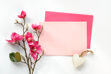 Blank postcard with envelope. Pink decorative magnolia flowers. Top view on off white background....
