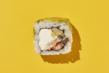 sushi roll with eel, pineapple, cheese, avocado on yellow.