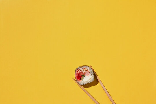 Fresh sushi roll and chopsticks on yellow background.