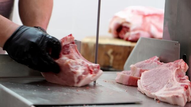 The butcher cuts pork ribs with special saw machine at meat processing plant, close-up 4K footage