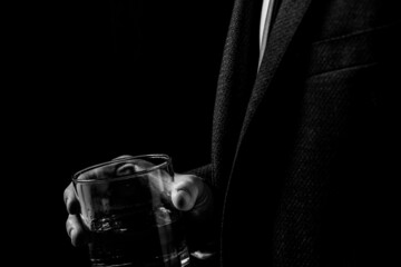 A glass of whiskey in the hands of a man in a suit in the dark, a man drinks