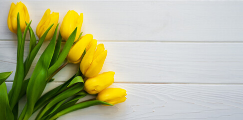 Flatlay composition with bouquet of beautiful yellow tulips on a white wooden background. Banner. Greeting card. Top view. Place for your text.