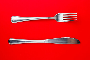 Top shot of silver fork and a knife on a bright red background.