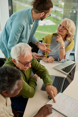 A multiracial group of elderly students is having a retraining course with a young teacher in the classroom.