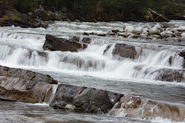 Waterfalls on a mountain stream with rocks and round stones