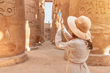 Travel blogger girl takes a pictures among columns of Hypostyle Hall at the ruins of the Karnak...