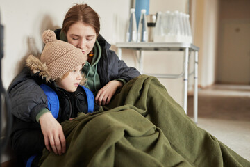Portrait of brother and sister hiding under covers in refugee shelter, copy space