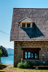 Vertical shot of a stone house with a dormer window near the scenic lake and mountains