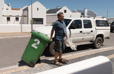 West Coast, South Africa. 2022.  Resident moving an empty green recycling bin from the highway onto his property.